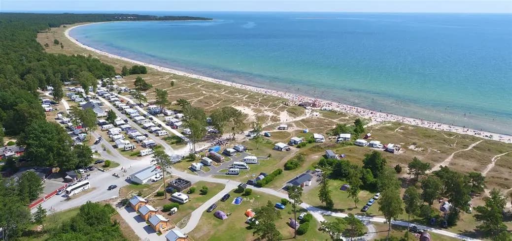 Flygfoto över Sudersand Resort med vy över stranden och bukten, där flera husbilar står parkerade nära stranden.