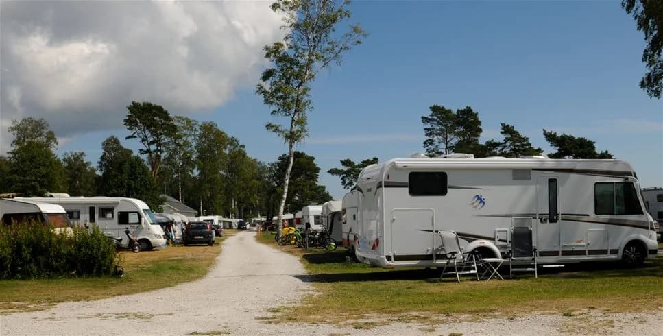 En campingplats vid Sudersand Resort med flera husbilar och campingfordon parkerade på gräsytor i närheten av träd och rekreationsområden.