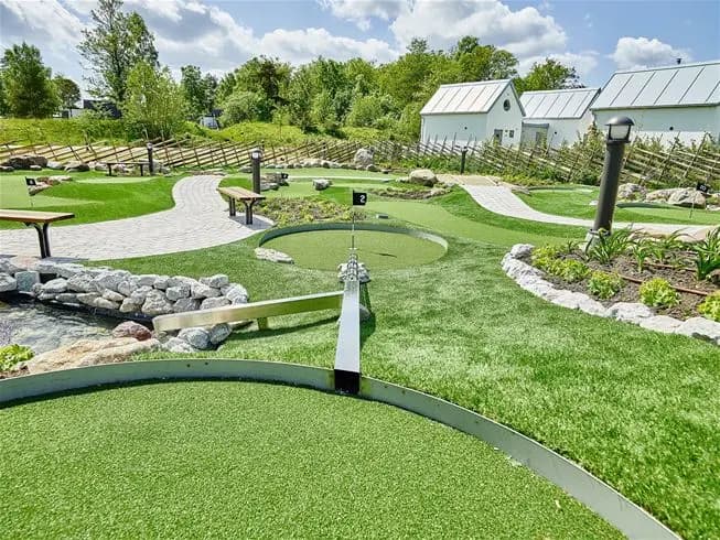 En grön och välskött minigolfbana med konstgräs, omgiven av grönt gräs och trädgårdslandskap, vid Sudersand Resort.