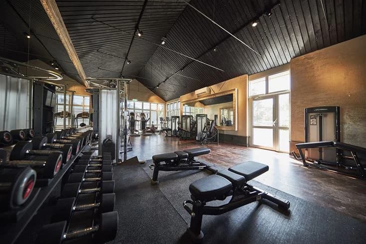 Ett modernt gym med trägolv och takbelysning, utrustat med olika träningsredskap och maskiner.