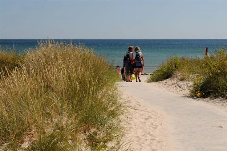 En solig strand vid Sudersand Resort med mjuk sand och klarblått hav. Flera besökare njuter av den natursköna kustmiljön och deltar i olika strandaktiviteter.