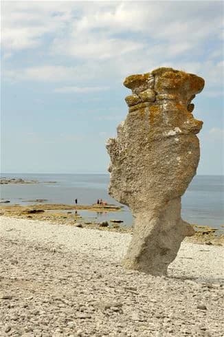 En solig dag vid Sudersand Resort med en vidsträckt sandstrand, kantad av klippformationer och vågor som slår mot kusten. Havet sträcker sig ändlöst i bakgrunden, vilket skapar en pittoresk och inbjudande atmosfär vid stranden.