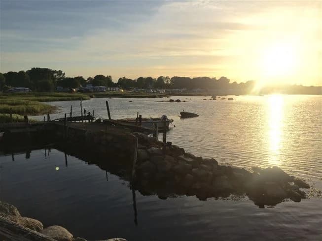 En vacker vy över Landöns camping vid skymning med en horisont där vatten möter himlen. Stenar syns vid strandkanten och kvällsljuset speglas i det stilla vattnet.