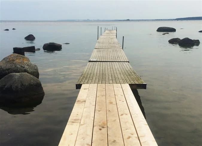 En träbrygga sträcker sig ut över vattnet vid Landöns camping, omgiven av kustnära landskap och hav.