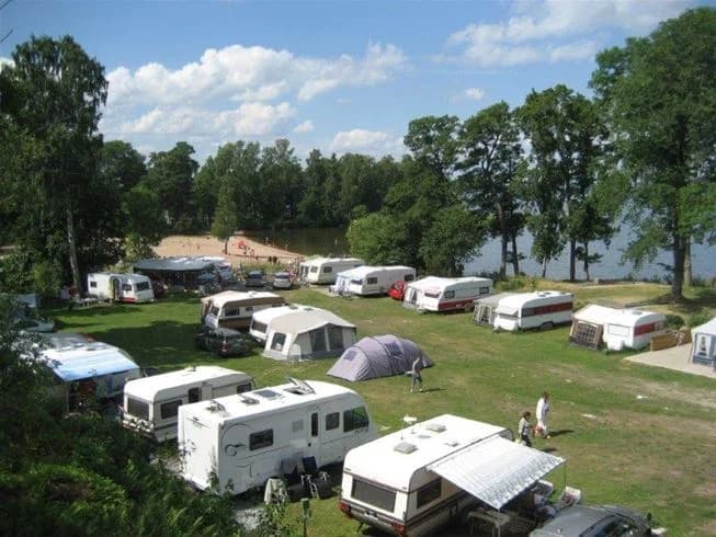 Flygfoto över naturskönt område med grönskande träd och campingplats. Flera husbilar och lastbilar ses parkerade vid platserna. I bakgrunden finns öppna landskap som sträcker sig mot horisonten.