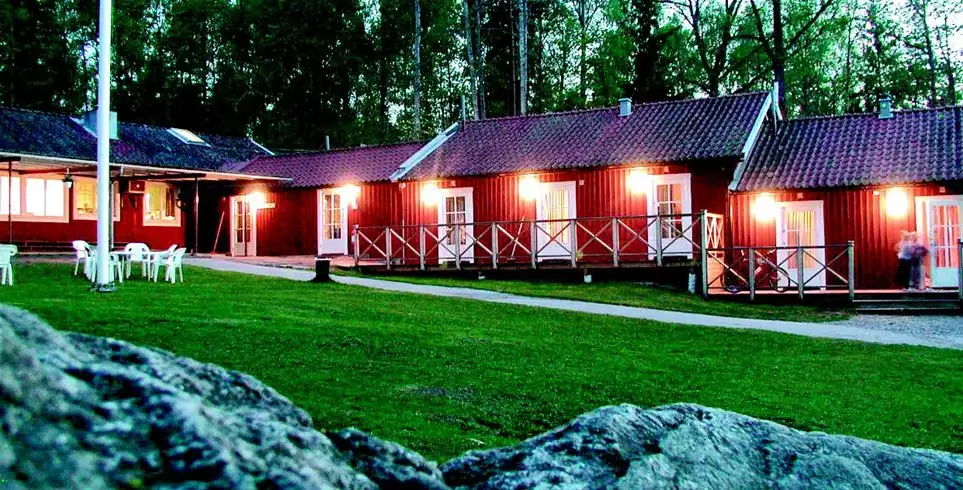 En mysig stuga omgiven av grönska med trädgårdsmöbler utomhus på altanen vid Hjälmargården & Läppe Camping, perfekt för en naturnära vistelse.