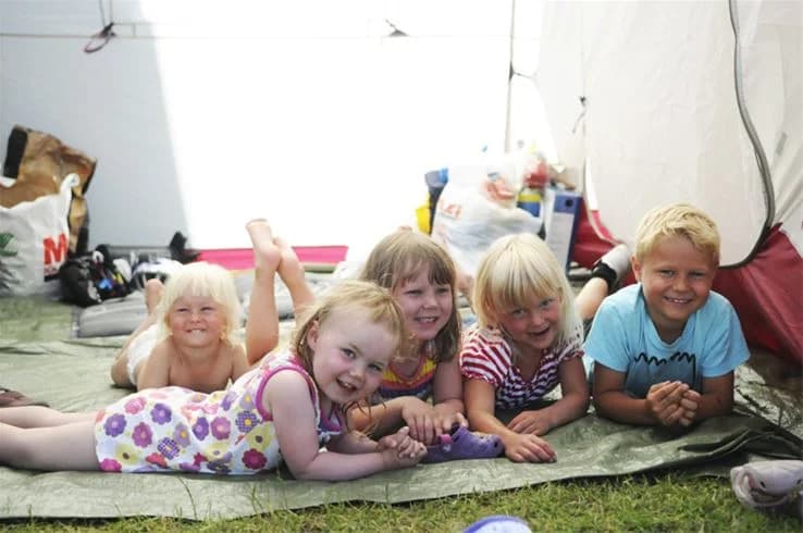 En grupp barn i sommarkläder sitter tillsammans på en gräsmatta och skrattar.