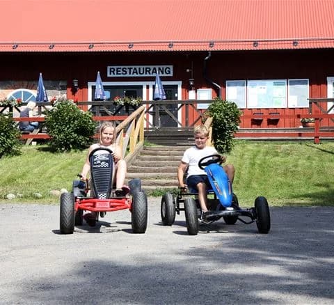 En leende pojke klädd för bad med en uppblåsbar badleksak vid stranden på Gålö Havsbad, omgiven av glada semesterfirare.