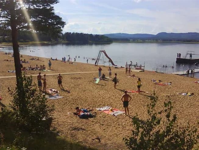 Strandvy vid Ljusdals camping med sjö och omgivande natur en solig sommardag.