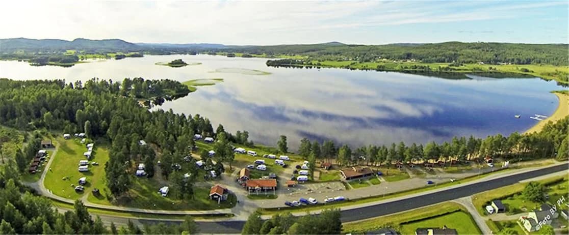 En lugn sjö vid Ljusdals camping med omgivande grönska och en grusstrand.