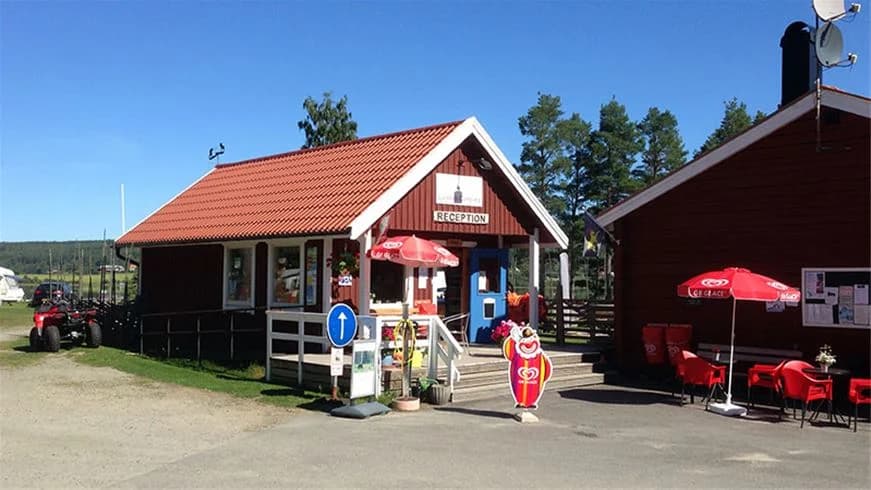 En viloplats vid Ljusdals camping med stolpar och picknickbord omgivna av grönska.