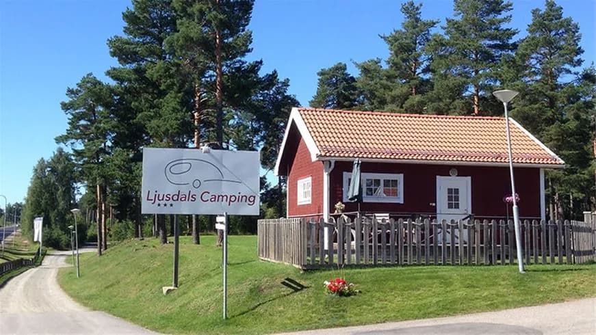En lantlig stuga omgiven av grönska med en välskött gräsmatta och en liten uppfart, belägen på Ljusdals camping.