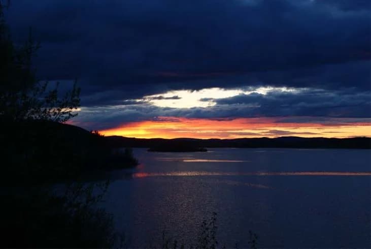 En vacker solnedgång över en kropp av vatten vid Ljusdals camping, med en klarblå himmel som speglas i vattnet och skapar en lugn och naturskön atmosfär.