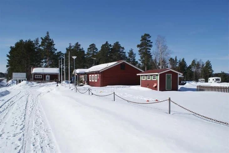 En vit vinterdag på Ljusdals camping med snöklädda stugor och skog, tak täckta av snö, en rofylld och pittoresk atmosfär.