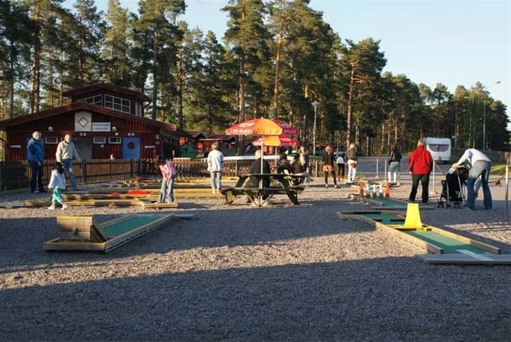En grupp människor njuter av fritidsaktiviteter på Ljusdals camping, omgiven av grönskande natur och blå himmel.