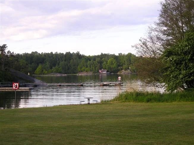 Bild av Järnaviks camping med en vacker vattenresurs omgiven av lummiga träd. Vattendraget reflekterar den gröna omgivningen, och en lugn sjö sträcker sig i bakgrunden. Perfekt för naturälskare och fridfulla utflykter.