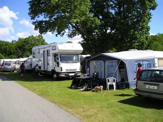 En bild av Järnaviks camping visar en öppen yta med flera parkerade husvagnar och tält. I bakgrunden syns träd och natur, vilket skapar en avkopplande campingmiljö.