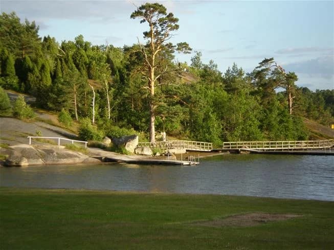 En naturskön vy över Järnaviks camping med stilla vatten, brygga och omgivande grönska, perfekt för friluftsliv och rekreation.