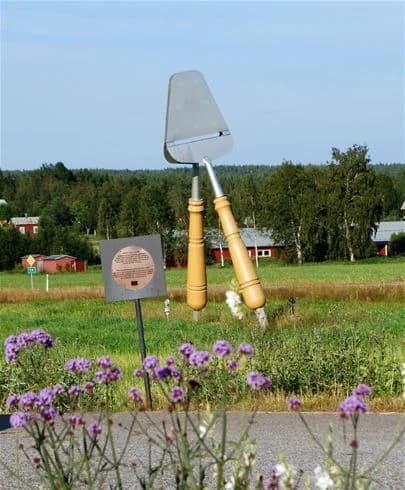 En vidsträckt jordbrukslandskap omgiven av öppna fält och vindkraftverk, med en camping och restaurang synlig i bakgrunden, vilket framhäver platsens naturnära och hållbara miljö.