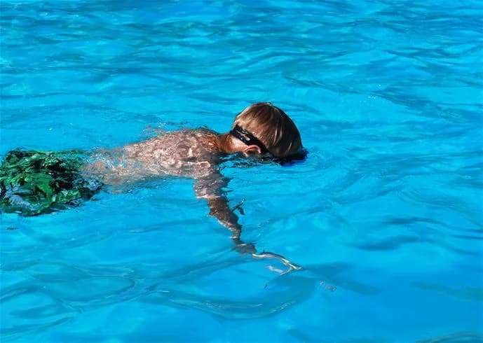En solig sommardag vid Lufta Camping & Restaurangs poolområde, med personer som simmar och har roligt i vattnet, några bär simglasögon.