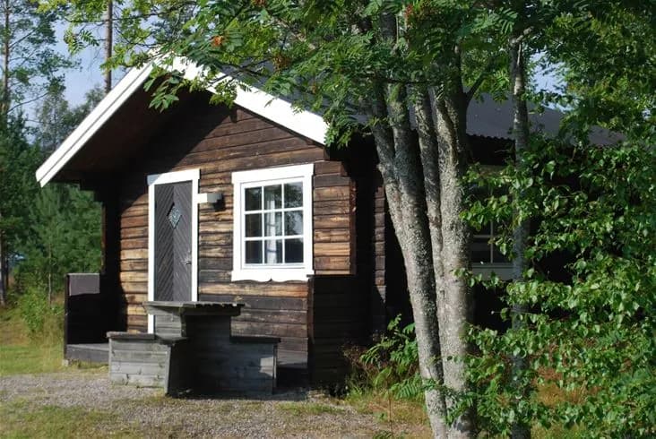 En trästuga med dörr och sidobyggnader, belägen i en lantlig miljö vid Lufta Camping & Restaurang.