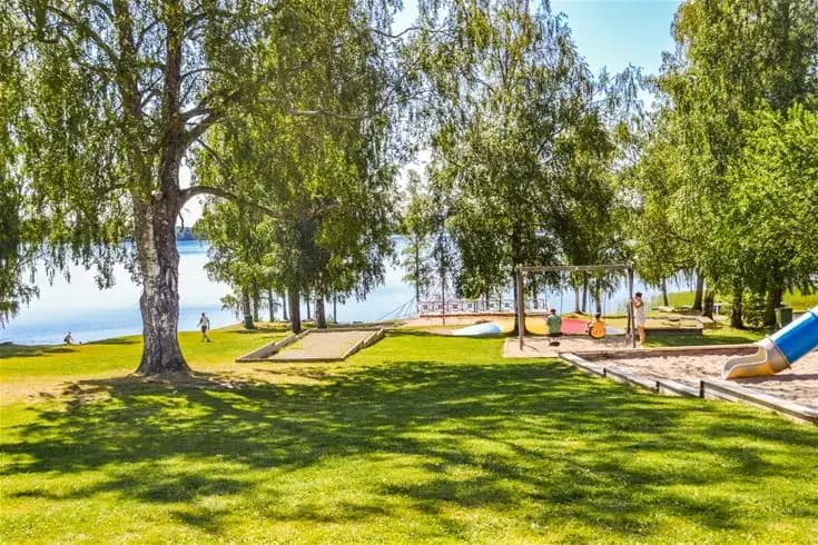 En grönskande campingplats med välklippta gräsmattor och skuggiga träd, omgiven av naturskön landskap i närheten av sjöar.