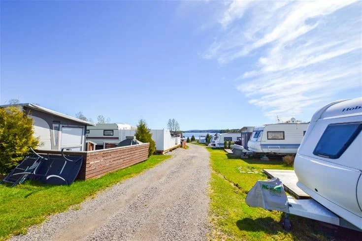 En husvagn parkerad vid kustlinjen på Charlottenberg camping & stugor - Haganäset, omgiven av grönska och med en vy över en vik i bakgrunden.