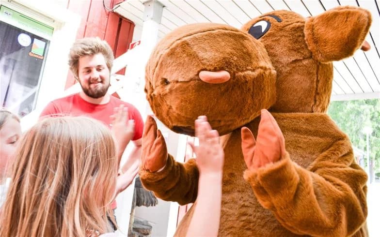 En grupp glada människor poserar med en maskot vid Charlottenberg camping & stugor – Haganäset, vilket skapar en stämning av semester och glädje.