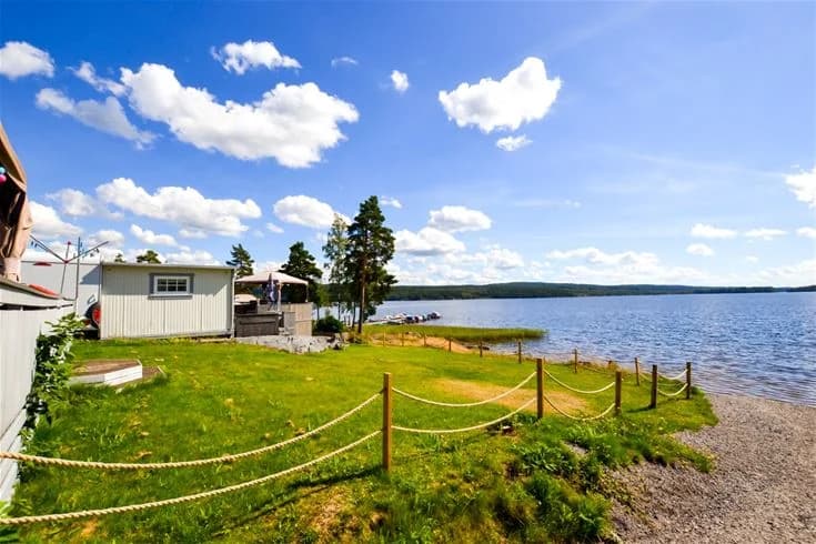 En naturskön campingplats vid en sjö, omgiven av grönskande gräsmattor och kullar, med en strandlinje i bakgrunden.