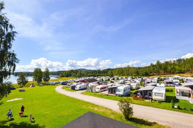 En vacker panoramautsikt över en sjö omgiven av grönska under en himmel med spridda cumulusmoln, vid Charlottenberg camping & stugor - Haganäset.