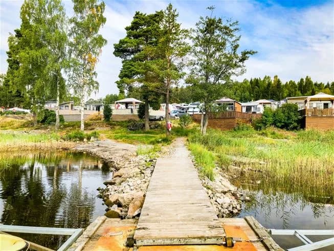 En naturskön miljö vid Charlottenberg camping & stugor - Haganäset, som visar en landskap med en fridfull damm, omgiven av grönska och öppna ytor, perfekt för avkoppling och utomhusaktiviteter.