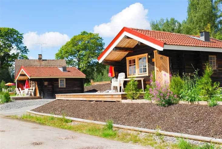 En idyllisk timmerstuga vid Charlottenberg camping omgiven av grönskande trädgård och gårdsbyggnader.