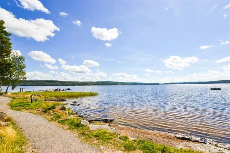 En naturskön vy över Charlottenberg camping & stugor - Haganäset, där en blå sjö sträcker sig mot horisonten under en himmel med vita moln.