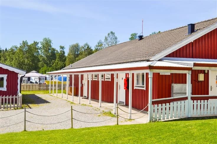 En skuggig campingplats med gräsbevuxen gård, belysningsstolpar och omkringliggande träd på Charlottenberg camping & stugor - Haganäset.