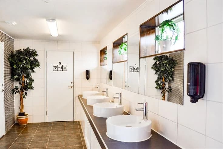 Ett modernt badrum på Charlottenberg Camping & Stugor - Haganäset, med stilren inredning, kaklade väggar och golv, ett handfat med blandare samt diskreta rördetaljer.