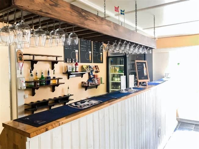 Interiör av Charlottenberg camping & stugor - Haganäset. Bilden visar en träinredd bar med hyllor fyllda med flaskor, träpaneler i tak och golv samt en bardisk i trä.