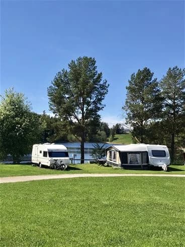 En campingplats med grön gräsmatta där flera husvagnar och husbilar står parkerade.