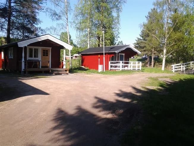 Bild av Stöde Camping med flera små stugor omgivna av grönskande gräsmattor och trädgårdsbyggnader. I förgrunden syns en uppfart och en välskött bakgård.