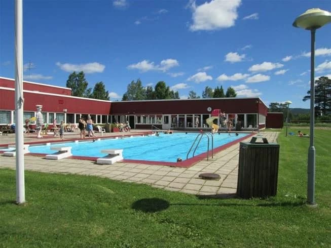 En campinganläggning med utomhuspool där gäster njuter av bad och avslappning. Solstolar är placerade runt poolområdet, med en semesterstämning på platsen. Perfekt för rekreation och avkoppling på semestern.