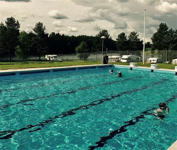 Bild av Stöde Camping som visar en badbassäng omgiven av gröna ytor. Flera besökare njuter av rekreation och vattensporter i en avslappnande miljö, vilket skapar en atmosfär av sommarsemester och fritid.