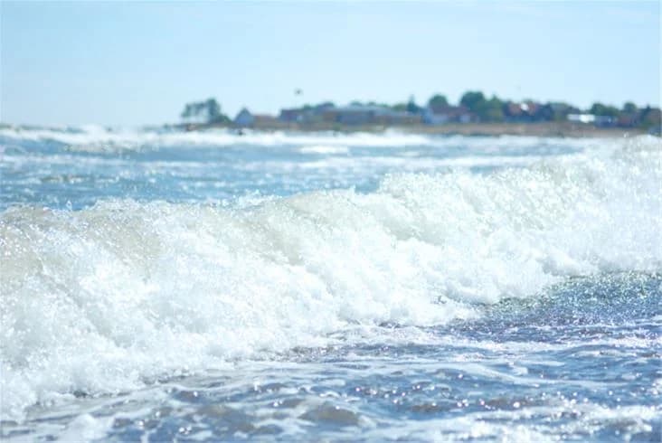 En solig dag vid kusten med blått hav och vitkappade vågor, Ljugarns Semesterby & Camping syns i bakgrunden.