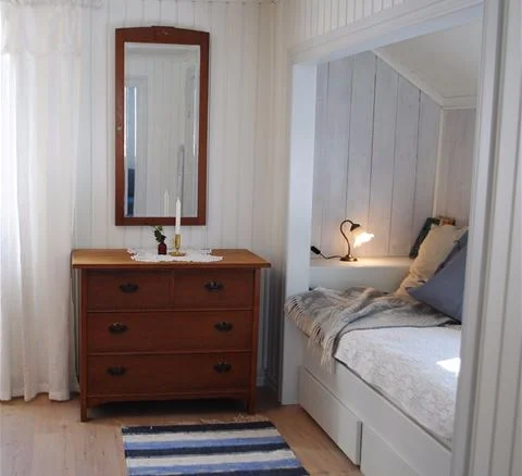 Ett mysigt sovrum på Anfasteröd Gårdsvik med en träinredning. Ett stort uppbäddat säng med vita lakan står centralt i rummet. Trägolv och ljusa väggar kompletterar den ombonade atmosfären.