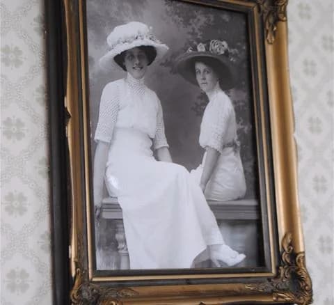 Svartvit fotografi av en person klädd i vintagekläder med en huvudbonad, omgiven av en dekorativ fotoram i retrostil, med anknytning till Anfasteröd Gårdsvik.