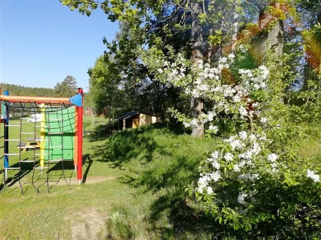 En grönskande trädgård i Yxningens camping med blommande äppelträd och välskött gräsmatta, omgiven av frodig växtlighet i vårens härliga atmosfär.