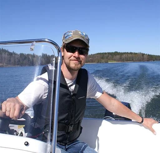 En motorbåt ligger förtöjd vid en brygga på Yxningens camping, med klarblått vatten och grönskande omgivning i bakgrunden. Solglasögon och fritidsutrustning finns på båten, vilket framhäver den avslappnade atmosfären och möjligheten till rekreation och båtliv på sjön.