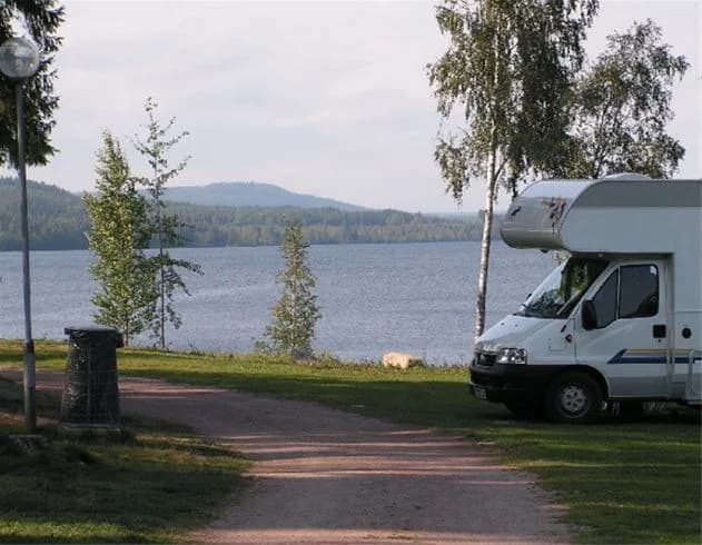 En husbil parkerad vid Munkebergs camping, med en sjö i bakgrunden omgiven av grönska.