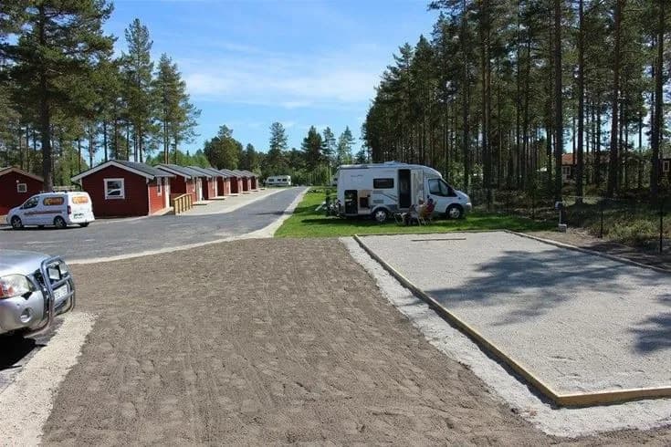 En trevlig campingplats med stugor omgivna av grönska och barrträd. En grusväg leder in till området där det finns både stugor och mobila hem, samt välskötta gräsmattor och anlagda växter.