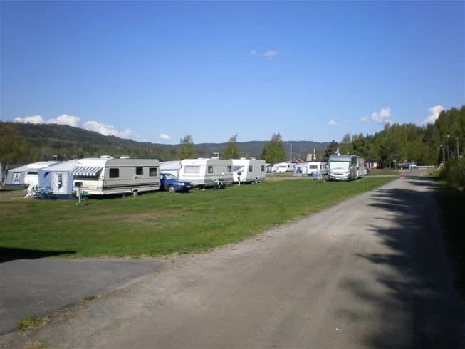 En husbil parkerad på Kävsta camping under en molnig himmel. I bakgrunden syns fler campingfordon och en vidsträckt natur.