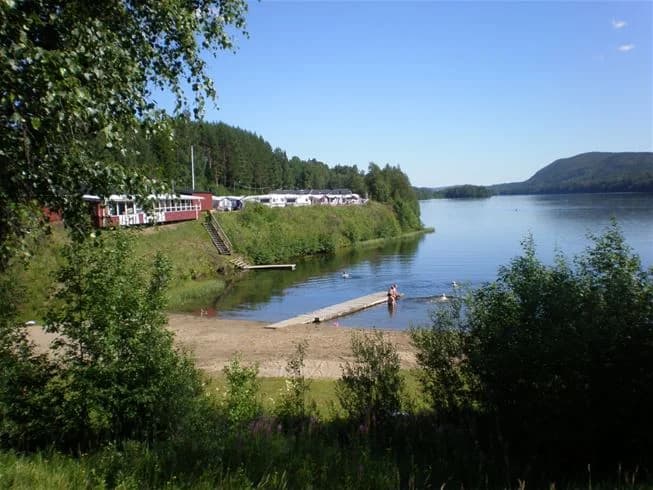 Vy över Kävsta Camping med en vattenväg som rinner genom landskapet, omgiven av grönskande flodbanker och reflekterande vattenytor, vilket skapar en fridfull och idyllisk naturmiljö.