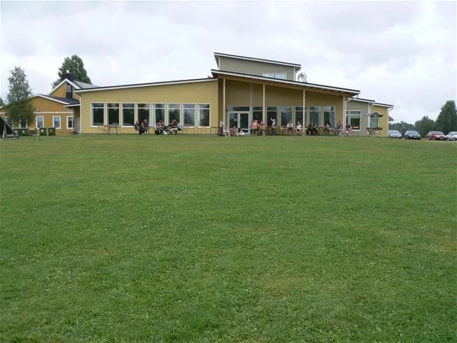 Bilden visar ett vidsträckt gräsområde vid Storstrand kursgård, som är idealiskt för rekreation och fritidsaktiviteter. I bakgrunden syns en lummig parkmiljö med fält och äng, vilket skapar en inbjudande atmosfär för besökare.